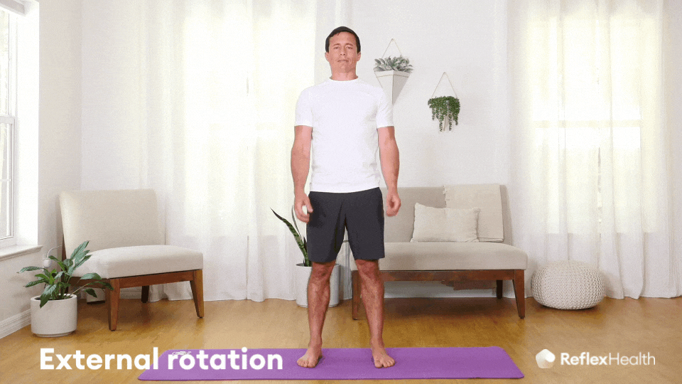 A man stands facing the camera, hands by his sides. He bends his elbows to 90 degrees, hands towards the camera. Keeping his elbows in position, he moves his hands away from each other, performing the External Rotation exercise.