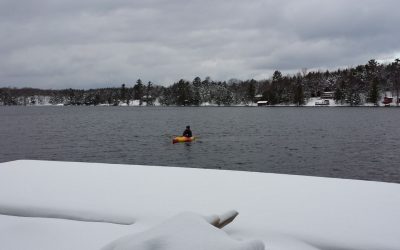 Photo of the author in a kayak with snow on the shore in the foreground