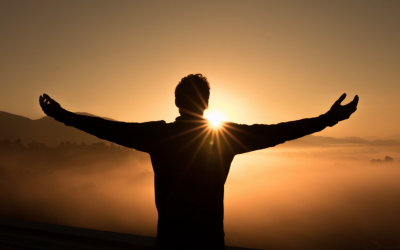 Silhouette of a person with arms outstretched overlooking sunset over mountains